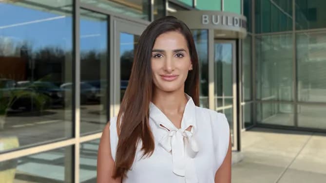 Nas is standing outside an office building's reflective windows, in a white shirt, smiling. 